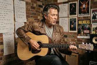 Musicien jouant de la guitare acoustique dans une salle de répétition avec des paroles manuscrites au mur, évoquant l'univers de Renaud et la chanson Lola